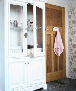 White bathroom, large white display cabinet, varnished wood door, pink towel, grey floor tiles. Pub orig IH 02/2009 Real home